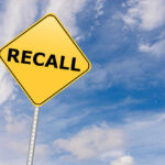 Yellow sign with RECALL text against blue sky.