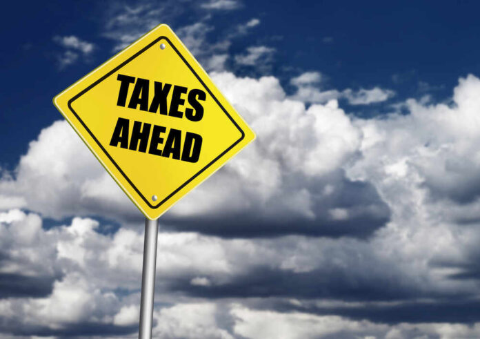 shutterstock_233717710.jpg featured image Yellow road sign reading taxes ahead clouds background