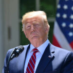 Donald Trump speaking with US flag in the back.