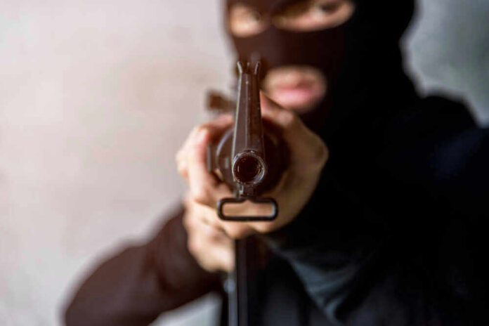 Person in balaclava aiming rifle at the camera
