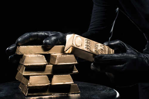 A person in black gloves handling gold bars against a dark background