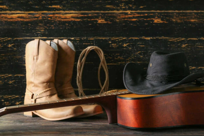 shutterstock_2338150313.jpg Cowboy boots, hat, and guitar on wooden surface