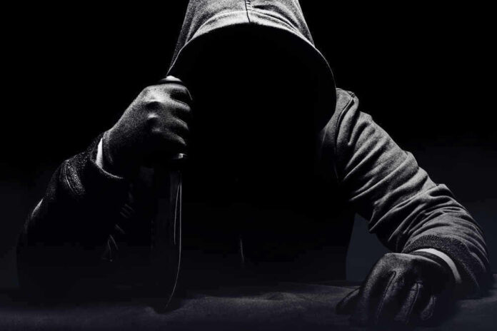 Person in dark hoodie holding a knife ominously