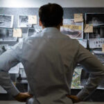 Man examining investigation board with photos and notes.