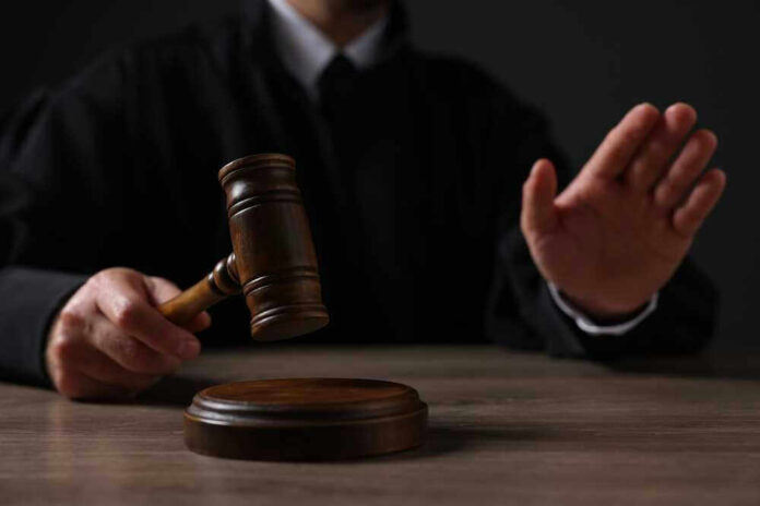 Judge holding gavel, hand raised in courtroom.