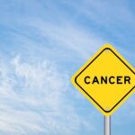 Yellow warning sign displaying the word 'CANCER' against a blue sky
