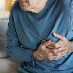 Man clutching chest in pain, sitting on couch.