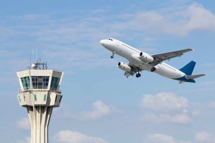 shutterstock_2298605343.jpg An airplane taking off near an airport control tower