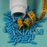 Revolutionary Obesity Pill Revealed Spilled blue capsules and a measuring tape on a turquoise background