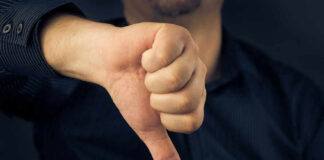 Hand showing thumbs down gesture, dark background.