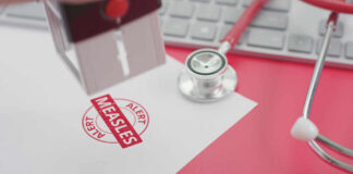 A stamp marking 'MEASLES ALERT' on a piece of paper next to a stethoscope and keyboard