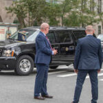 Trump Motorcade REROUTED After Alarming Discovery Two security personnel monitoring a convoy of black SUVs in an urban area