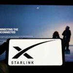 A hand holding a smartphone displaying the Starlink logo in front of a screen showing a connectivity message