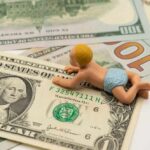 A baby figurine crawling on top of various dollar bills