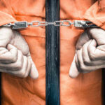Felon KILLS Innocent Neighbor Through Wall Handcuffed person in orange jumpsuit behind prison bars.