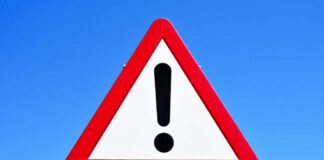 A triangular warning sign with an exclamation mark against a blue sky