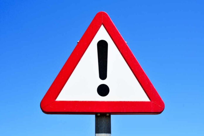A triangular warning sign with an exclamation mark against a blue sky