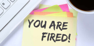 A sticky note with the message 'YOU ARE FIRED!' placed on a desk next to a keyboard and a cup of coffee