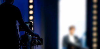 Person being filmed on a set with lights.