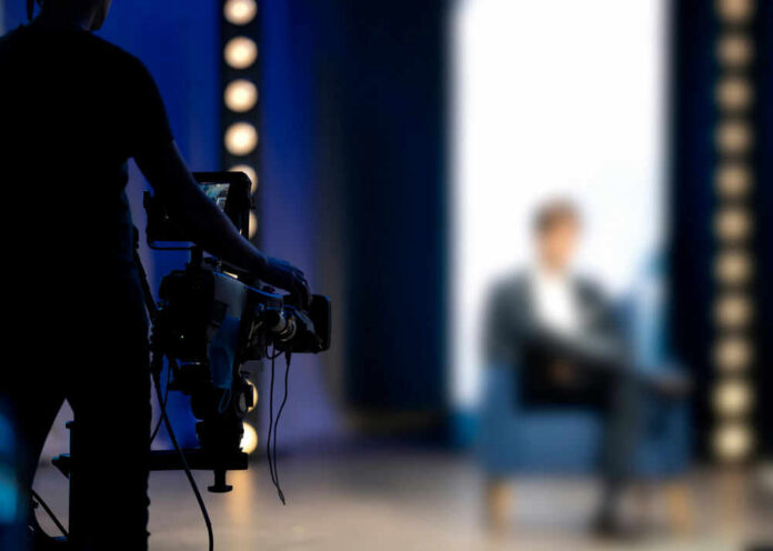 Person being filmed on a set with lights.
