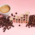 Coffee Apocalypse: Will Prices EVER Drop? A cup of coffee next to wooden blocks with upward arrows and scattered coffee beans on a pink background