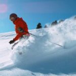 A skier in a red jacket skiing through fresh snow