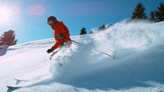 A skier in a red jacket skiing through fresh snow