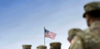 Soldiers in uniform with American flag in background.