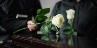 Two individuals placing white roses on a coffin during a funeral