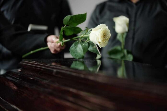 Two individuals placing white roses on a coffin during a funeral