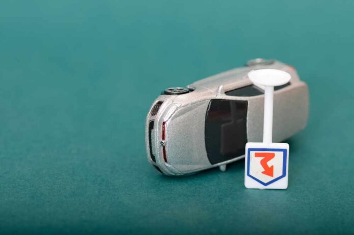 A silver toy car next to a small road sign