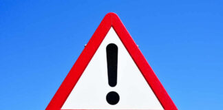 A triangular warning sign with an exclamation mark against a blue sky