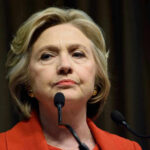 Hillary Clinton in a red blazer at a podium.