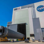 1,300-Pound NASA Satellite Plunges to Earth Massive rocket component outside NASA assembly building under clear sky.