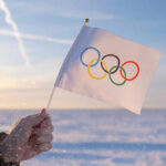 Trump Forces Olympics To Change Policy Hand holding Olympic flag in snowy landscape