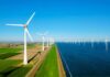 A row of wind turbines along a coastal area with fields and blue sky