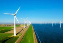 A row of wind turbines along a coastal area with fields and blue sky