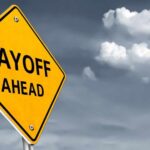 Yellow warning sign indicating layoffs ahead against a cloudy background