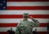 A military personnel saluting in front of a large American flag