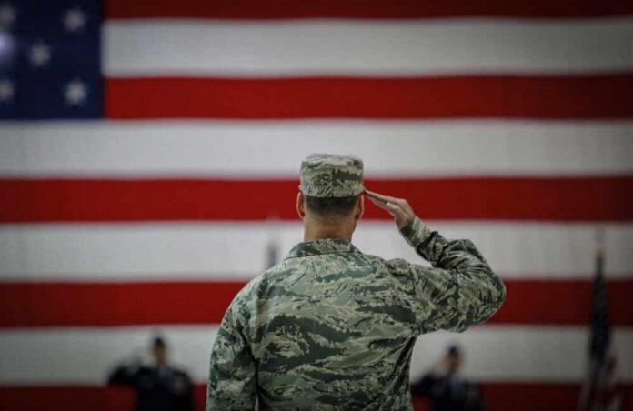 A military personnel saluting in front of a large American flag