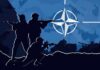 Silhouettes of soldiers with weapons against a blue background featuring the NATO emblem