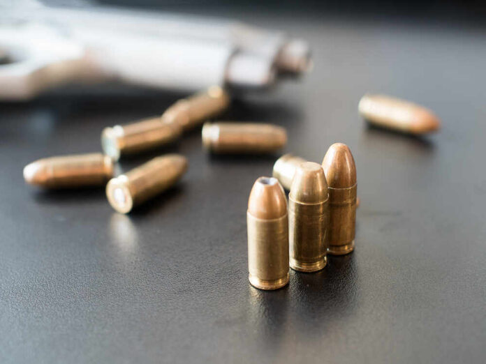 Close-up of bullets on a dark surface with a handgun in the background