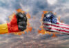 Two fists, one painted with the German flag and the other with the American flag, clashing against a fiery background