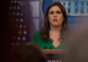 Sarah Huckabee Sanders speaking at a press conference podium.