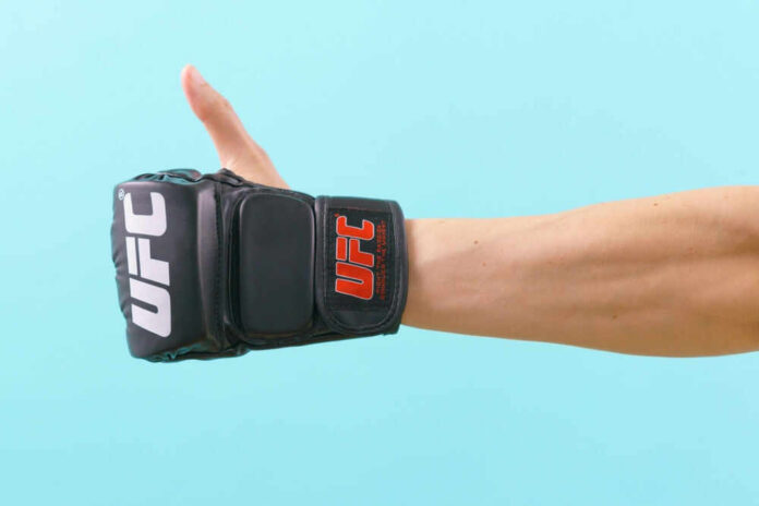 shutterstock_2189717391.jpg Thumbs up with UFC gloves, blue background.