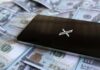 A smartphone placed on a pile of hundred-dollar bills