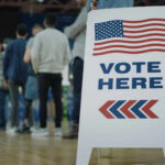 National Voter List Sparks Constitutional Showdown People in line next to Vote Here sign