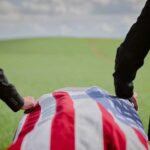 Senator’s Daughter DEAD at 36 — Decades-Long Battle Two individuals standing beside a flag-draped casket in a green field