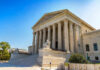 Supreme Court Axes Map: Chaos Ensues! Stone building with columns and statues, clear blue sky.