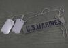 Military dog tags and a U.S. Marines name tape on a green background